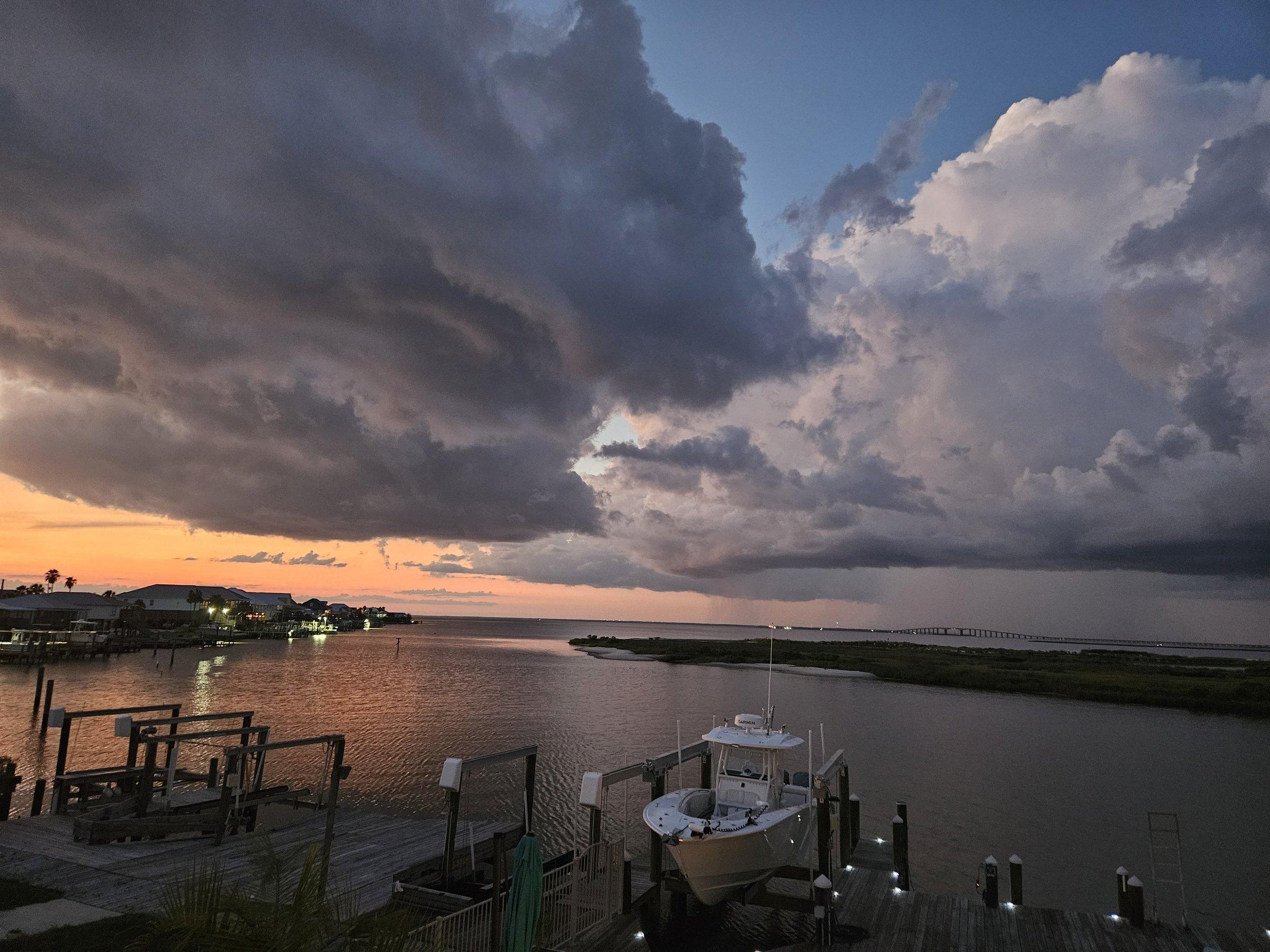 Dramatic storm clouds break over Mobile Bay at sunset, with a boat resting on its lift.