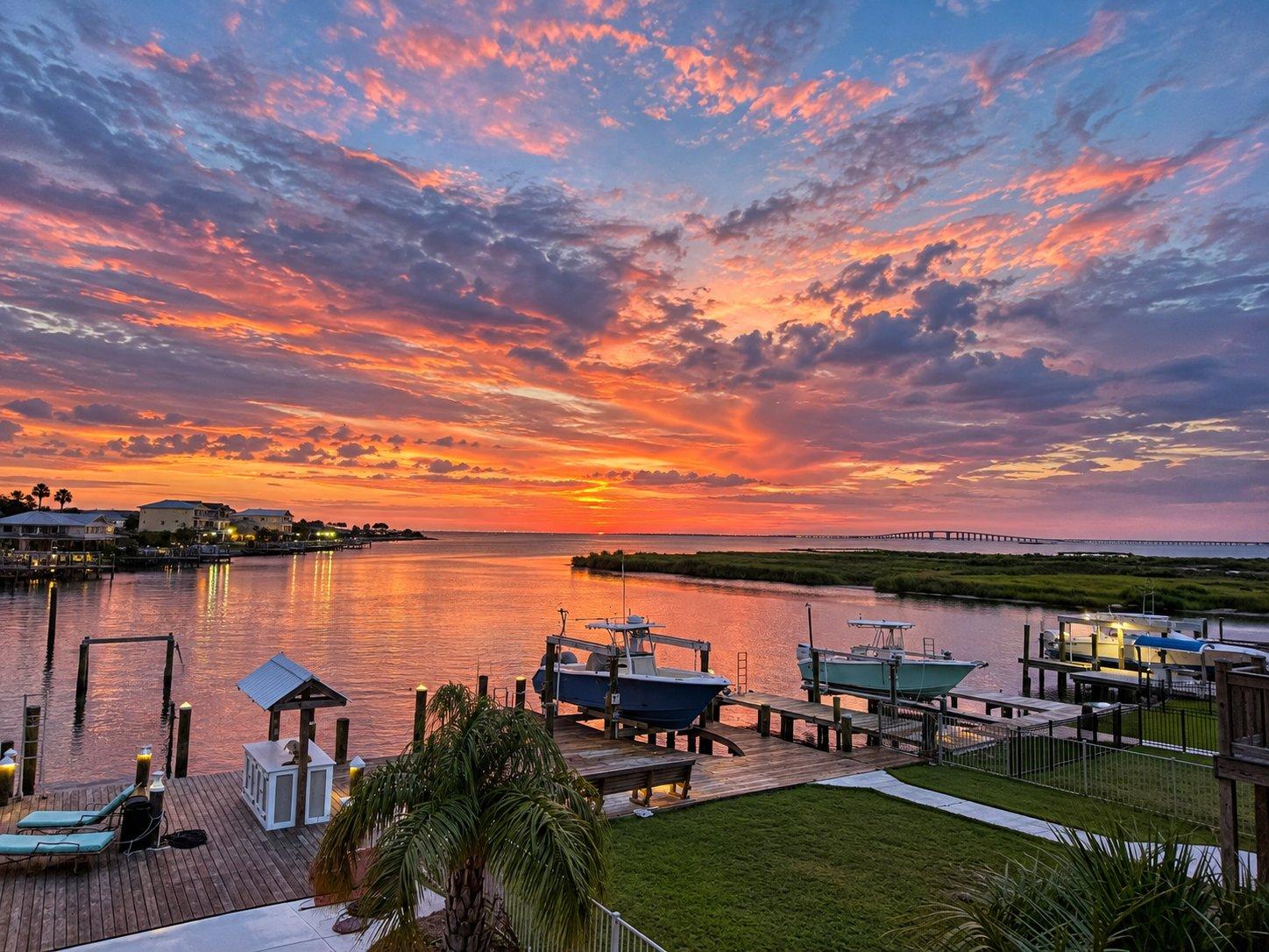 A dock stretches out over calm water at Mobile Bay under a warm sunset sky.